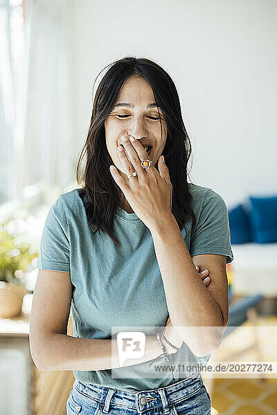 Happy woman with eyes closed covering mouth at home