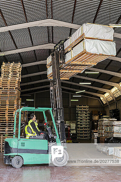 Forklift worker carrying wood pallets at warehouse