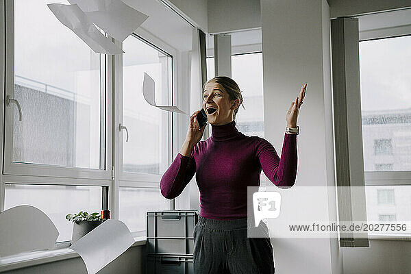 Excited businesswoman throwing papers in air at office