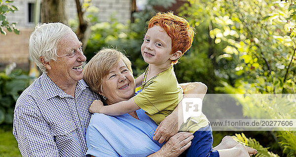 Happy senior couple having fun with grandson in garden