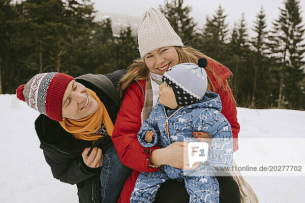 Smiling woman with baby boy near man in winter forest