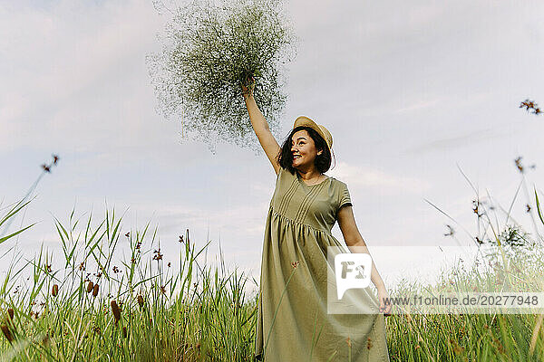 Happy woman wearing dress and holding gypsophila flowers in field