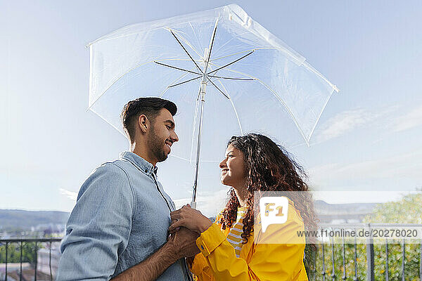 Romantic couple standing under umbrella on balcony