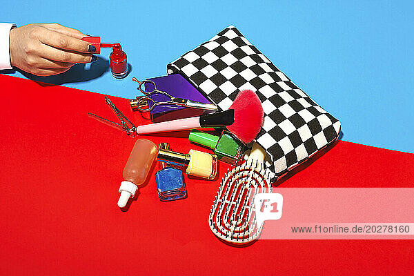 Studio shot of female hand touching cosmetics falling out of checked purse