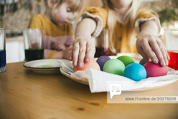 Girl arranging colorful Easter eggs in plate on table at home