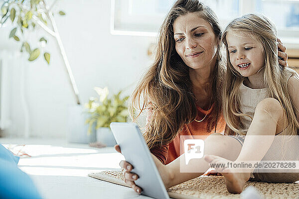 Smiling girl using tablet PC with mother at home
