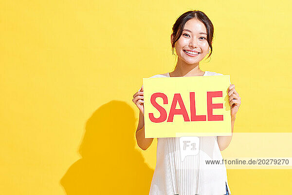 Asian woman holding up sale sign on yellow background