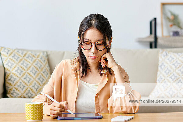 A woman in glasses sitting at a table with a tablet and pen