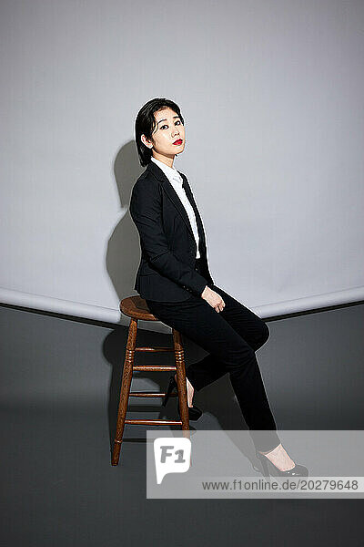 A woman in a suit and heels sitting on a stool