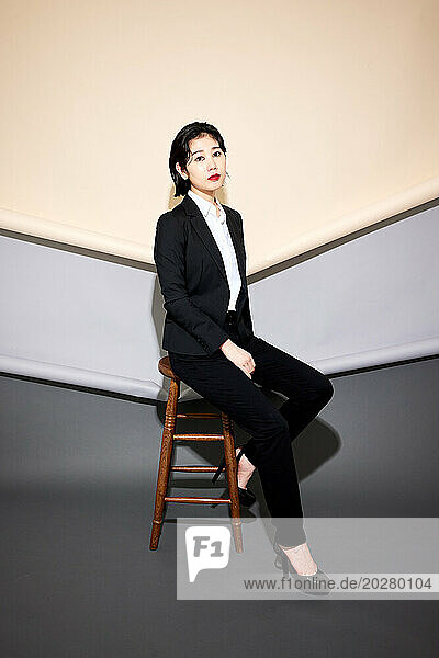 A woman in a suit sitting on a stool