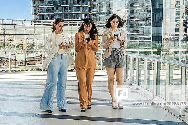 Drei Geschäftsfrauen gehen im Freien spazieren und benutzen dabei Smartphones. Alle Frauen sind in Geschäftskleidung gekleidet