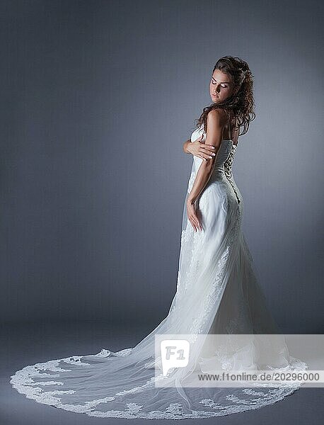 Schlanke Brünette posiert in stilvollem Hochzeitskleid  auf grauem Hintergrund