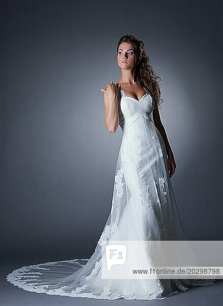 Schöne schlanke Braut posiert in eleganten langen Kleid  auf grauem Hintergrund
