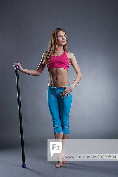 Studioaufnahme einer muskulösen  starken Frau mit Fitnessbar  auf grauem Hintergrund