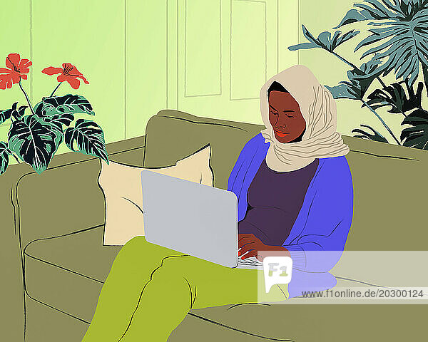 Muslim woman in hijab using laptop on living room sofa at home