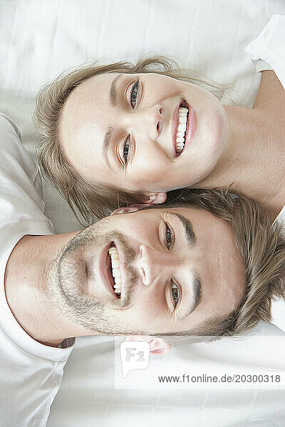 Smiling Couple Lying on Bed Facing Opposite Directions