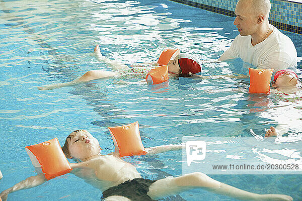 Children in Indoor Swimming Pool Learning to Swim with Instructor