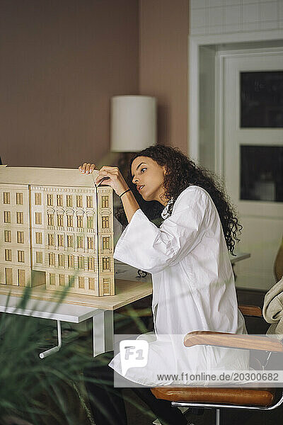 Side view of female architect making building model while sitting on chair at office