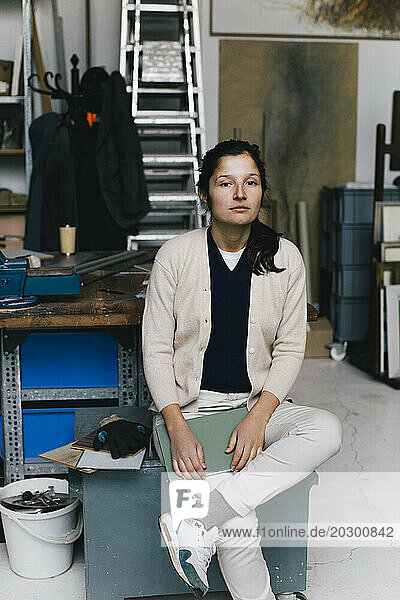 Portrait of businesswoman sitting on table in workshop