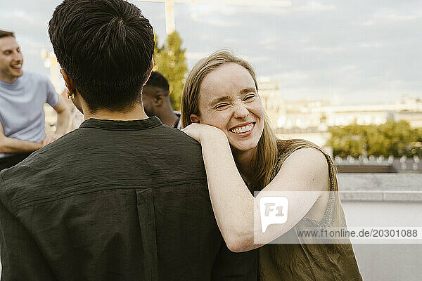 Portrait of smiling woman laughing while leaning on male friend's shoulder at party