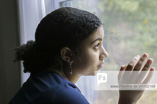 Biracial teen girl in profile looks out a window
