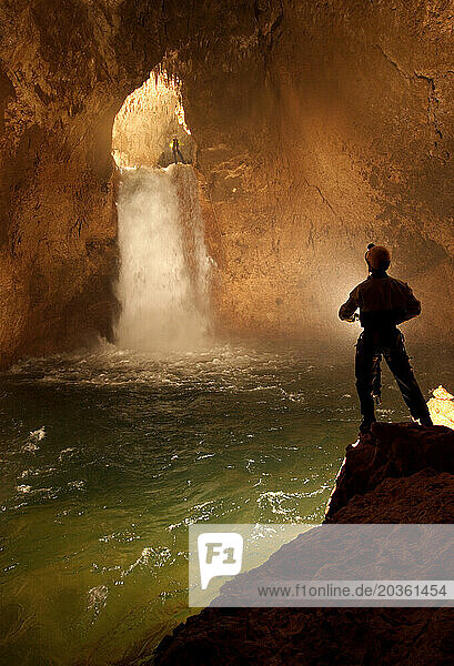 Cave explorers illuminate a large waterfall deep in a cave in New Britain