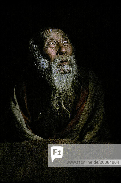 Nepalese blind buddhist monk sits under a small ray of light.