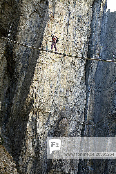 A young woman walking on a bridge while engaging in the sport of Via Ferrata in Val D'isere  Savoie  France.