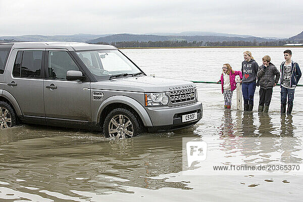 Children watching car driving through flooded street in Storth at Kent river estuary