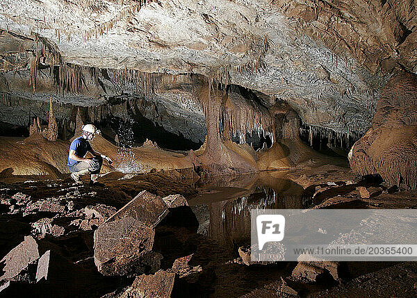 A cave explorer crouching by a pool of water in a cave in Mulu National Park.