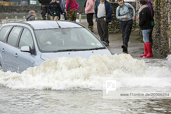 Car driving deep in water in flooded street in Storth at Kent river estuary
