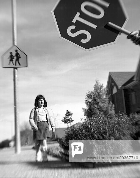 A little girl crosses the street on her way to school as an officer holds up a stop sign for oncoming traffic.