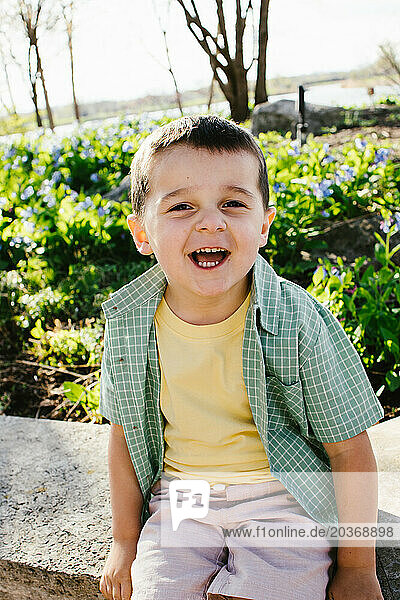 Young boy smiling happy in sunshine with spring flowers behind