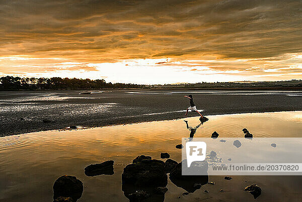 Child jumping from rock in water at sunset