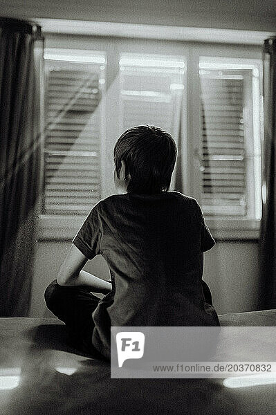 Boy on the bed with light shining through blinds in the pandemic