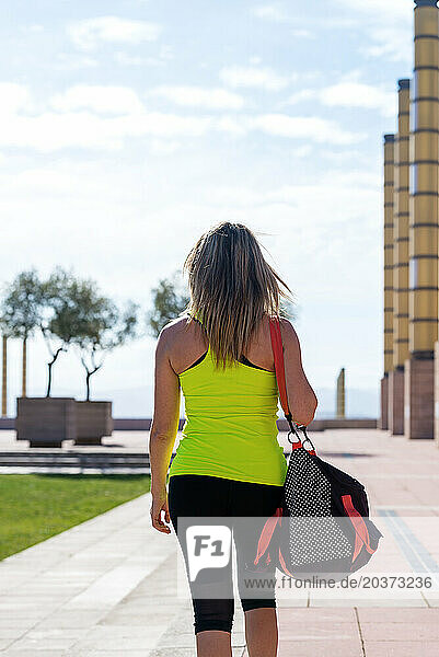 Rear view of mid adult woman  sports bag on shoulders walking outdoors