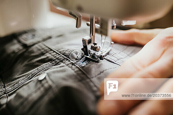 Man sits at kitchen table with sewing machine patching work pants