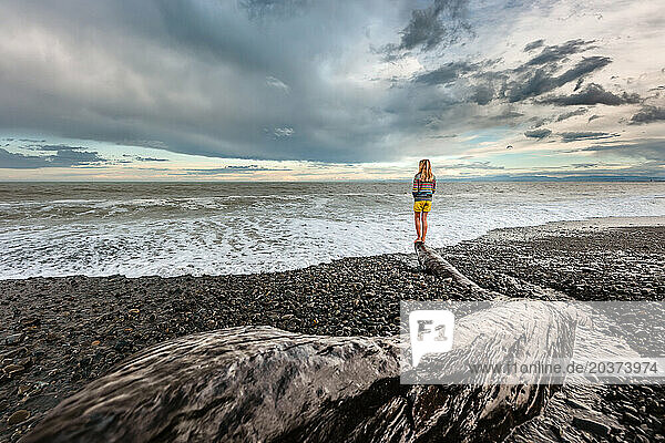 Girl standing on log at beach in New Zealand