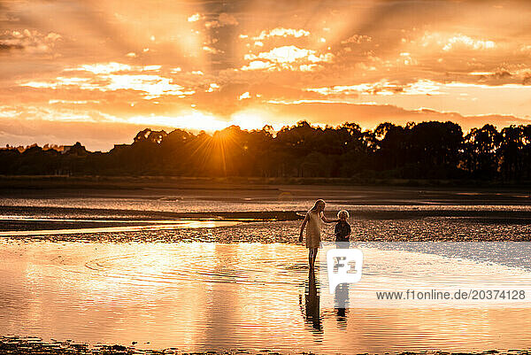 Siblings walking in water with beautiful orange sunset