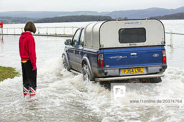 Woman watching car driving in flooded street in Storth at Kent river estuary