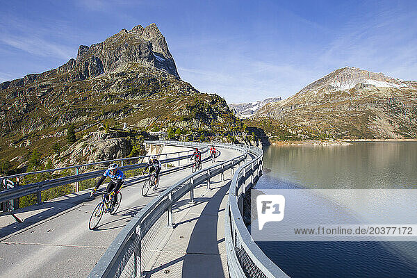 Four road bikers on the dam of the Emosson reservoir lake in the Alps on the border of France and Switzerland.