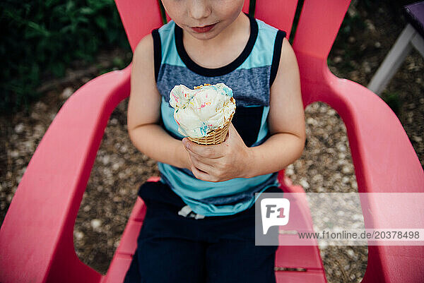 Overhead view of boy sitting in bright chair eating ice cream cone