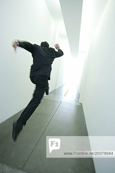 A man taking leaps down a long hallway towards a bright light at the end of it.