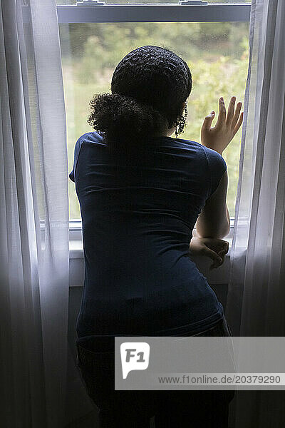 From behind  biracial teen girl looks out a window