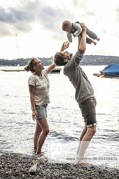 Happy couple holding daughter in mid air at lake