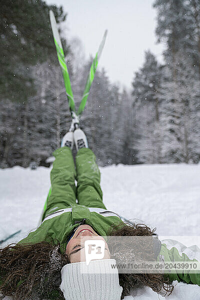 Young woman with legs in air lying on snow at winter forest