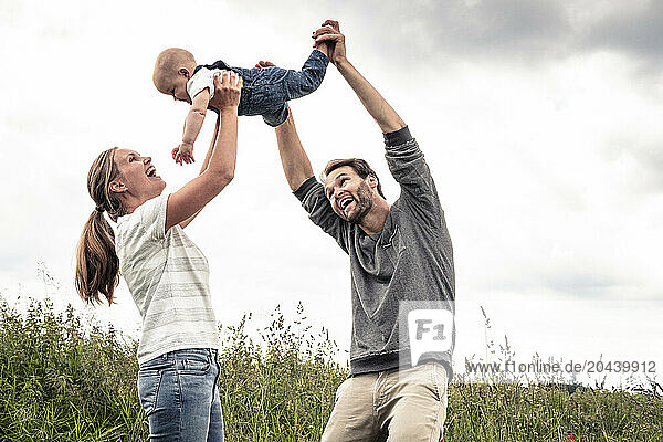 Father and mother holding daughter in mid air at meadow