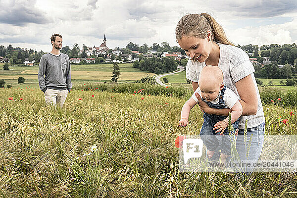 Smiling mother holding daughter and playing with flower at meadow