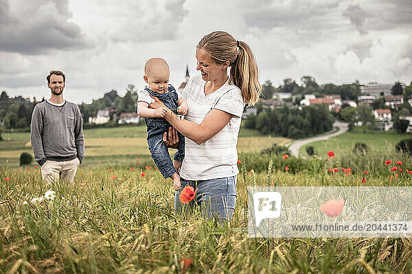 Mother carrying daughter in arms and standing near father in meadow