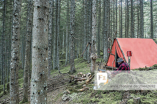 Senior man enjoying bonfire and cooking food near tent in forest